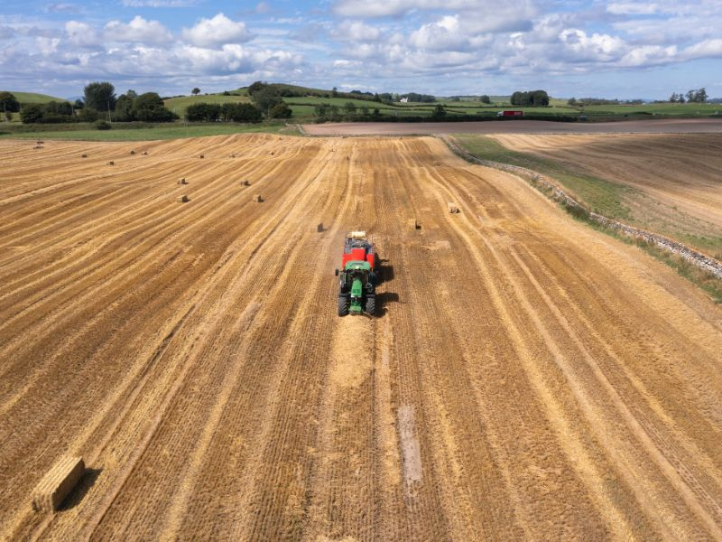 Aerial view of a tractor in a field towing a bailing machine making bales of straw after the cereal crop in the field was harvested
